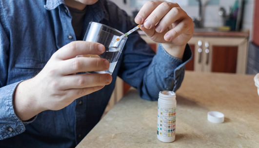 A man in the kitchen tests tap water quality with a test strip